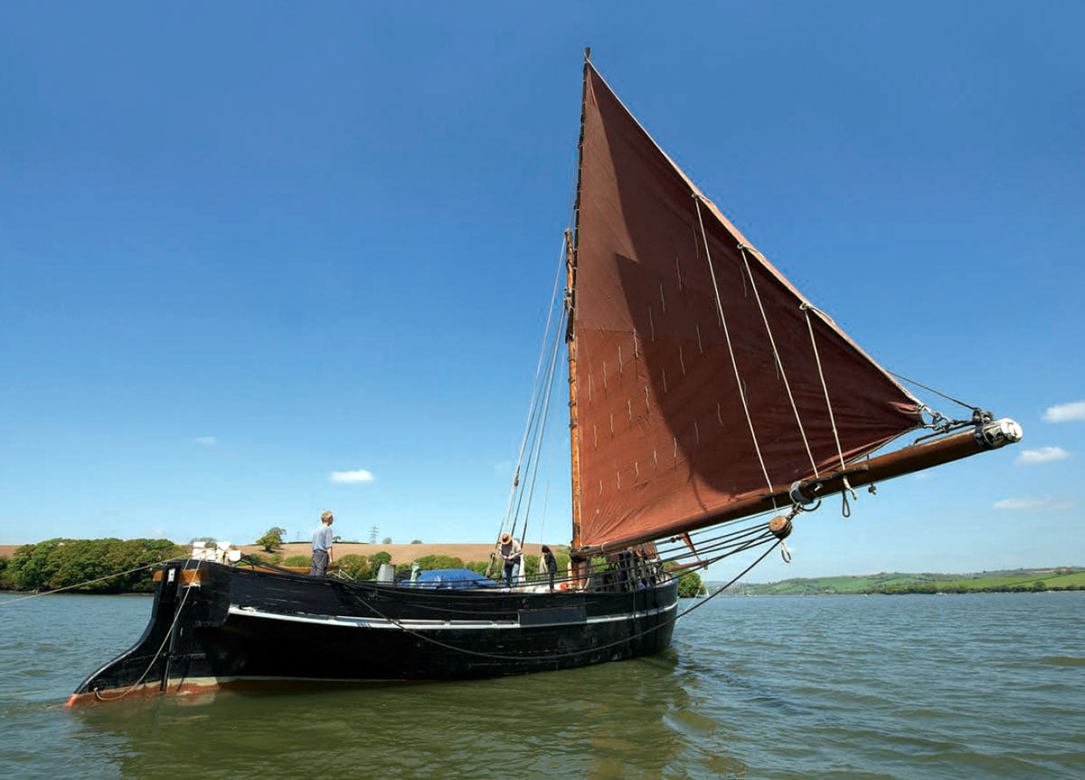 Wooden sail boat on the water with sailors aboard.