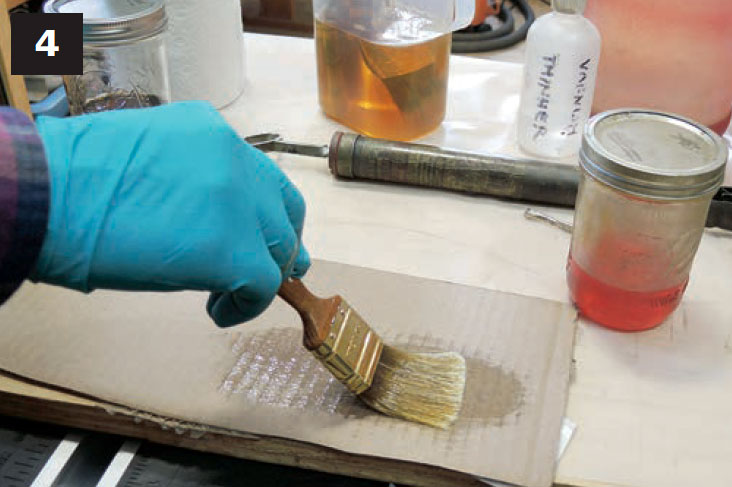 Hand using brush to test varnish on a piece of cardboard.
