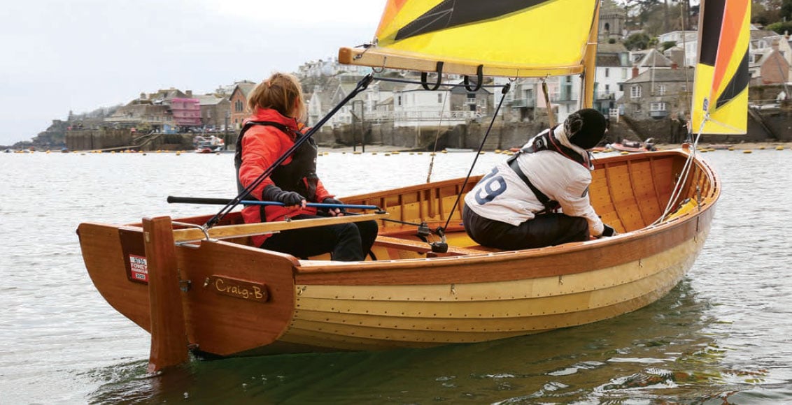 Two sailors aboard a Fowey River Boat with multi-color sails.