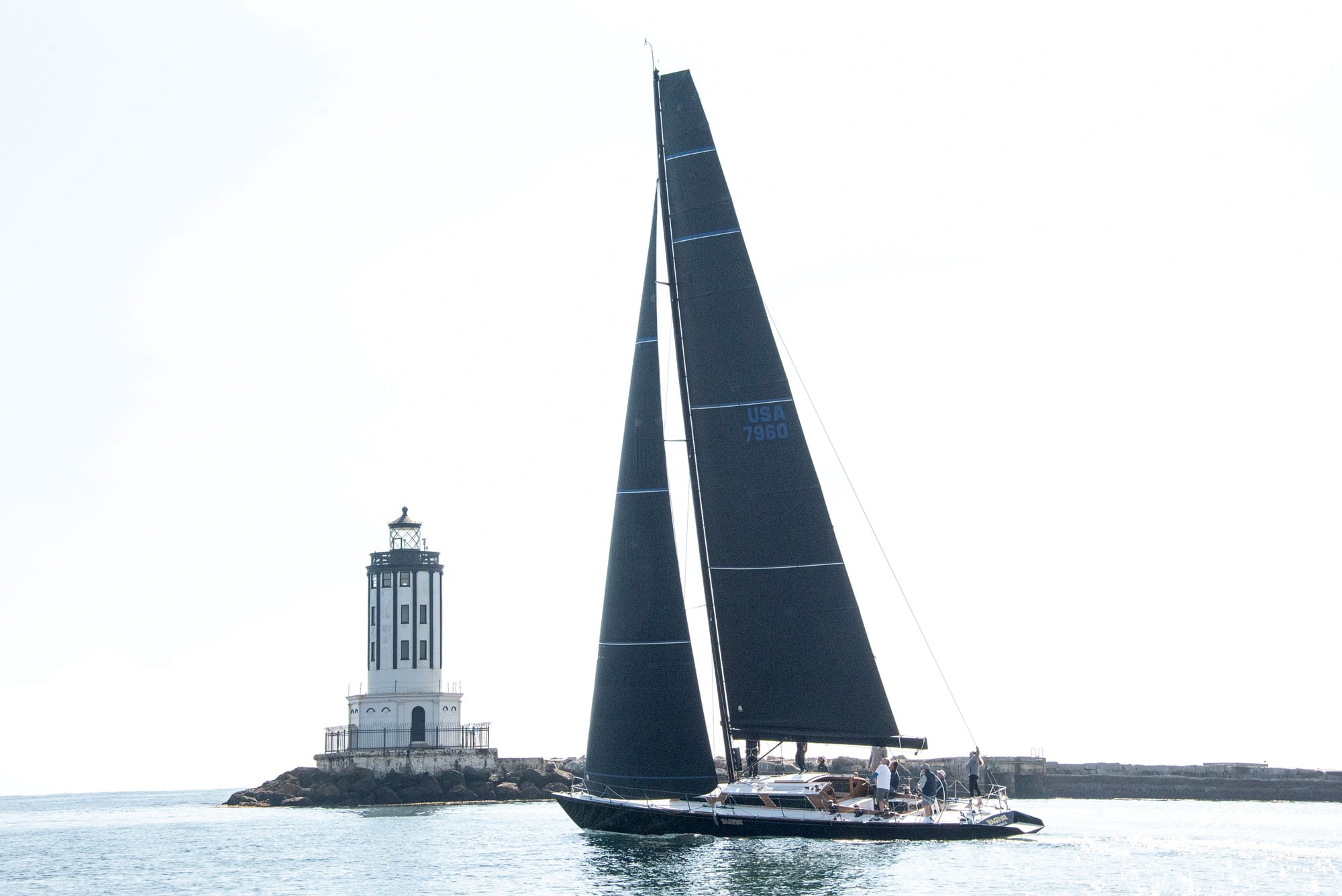 Sailing yacht in the ocean with a lighthouse in the background.