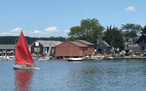 Small sailboat in water in front of a dock area.