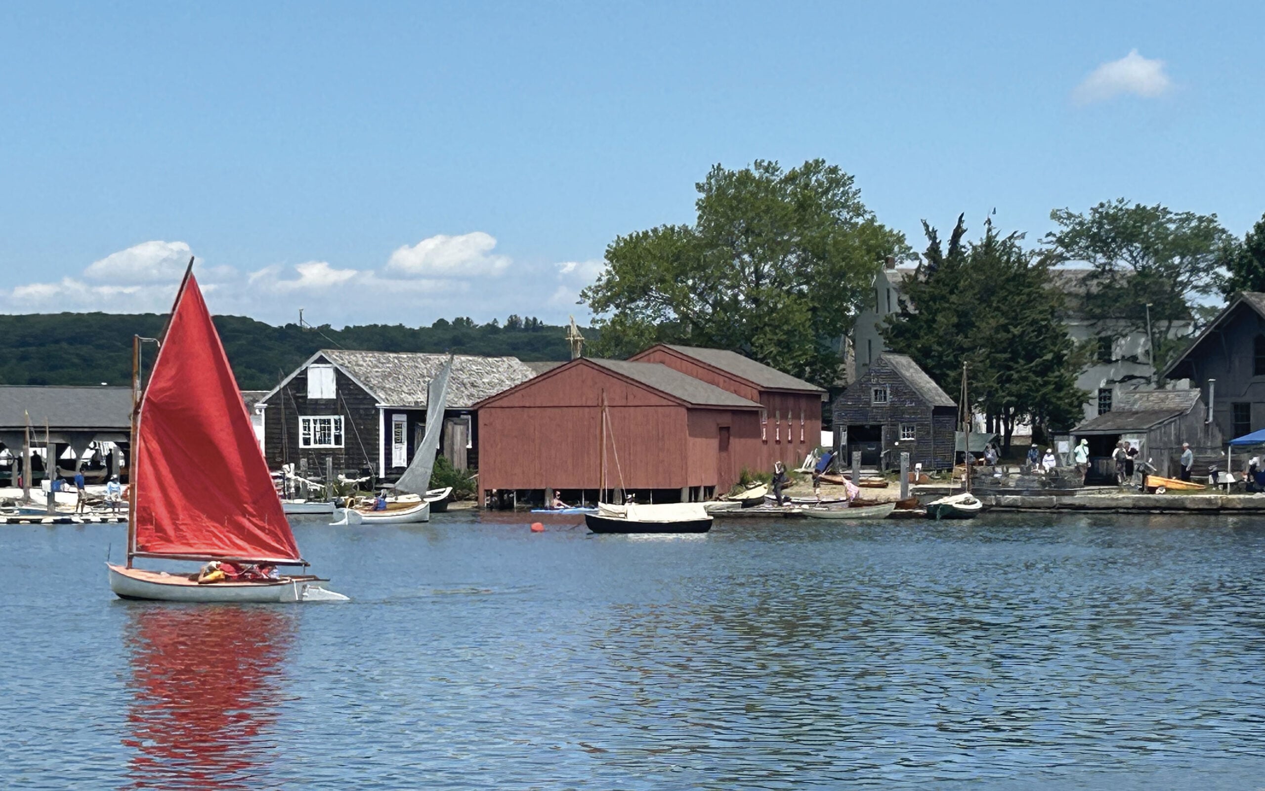 Small sailboat in water in front of a dock area.